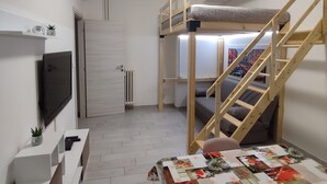 A compact room with a bunk bed, a TV mounted on the wall, a small desk with a plant, and a radiator. - Cozy apartment very close to metro and bus to visit Rome (Roma)