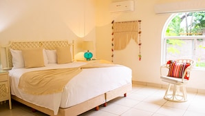 A neatly arranged bedroom with a large bed, bedside tables, a window with a view of greenery, and a chair with a colorful cushion. - Condo Palau by Kivoya (Nuevo Nayarit)