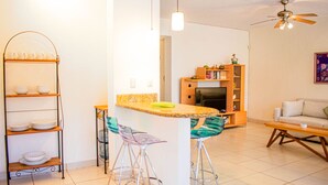 A modern kitchen with a central island, a dining area with a sofa, and a bookshelf. - Condo Palau by Kivoya (Nuevo Nayarit)