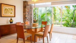 A dining area with a glass table surrounded by chairs, a stone wall, and a large window with a view of greenery. - Condo Palau by Kivoya (Nuevo Nayarit)