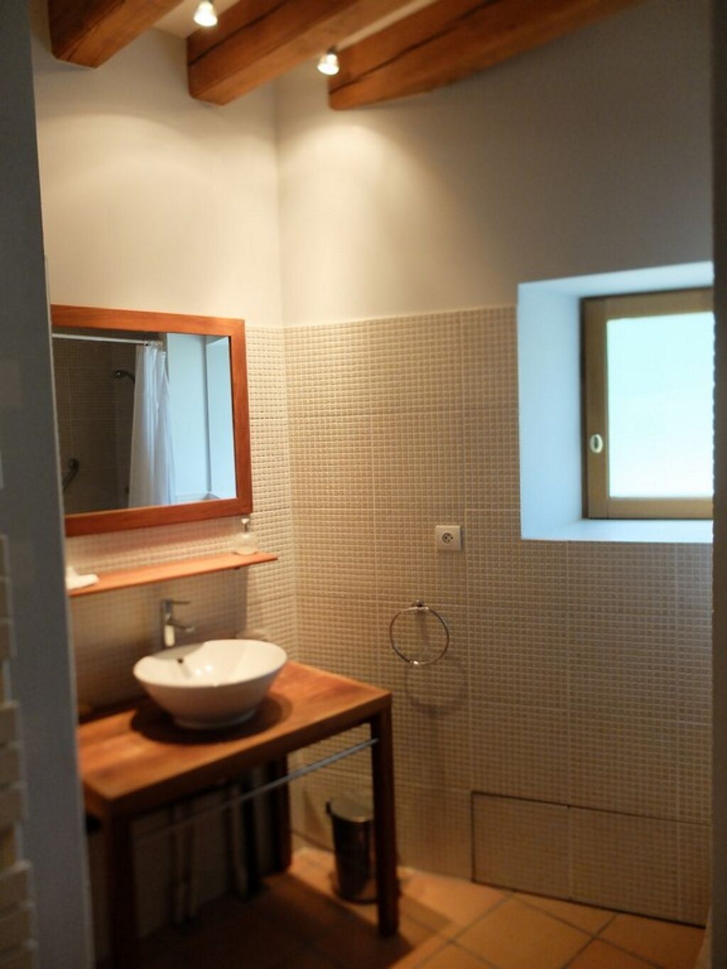 Une salle de bain avec un meuble-lavabo en bois, un lavabo blanc, un miroir, une douche et une fenêtre.