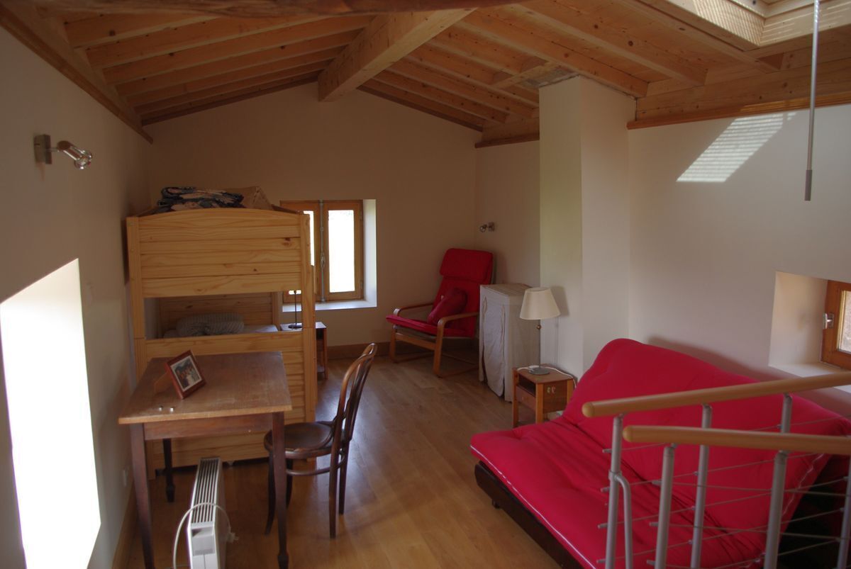 A cozy room with a bunk bed, a red sofa, a small table, and a chair.