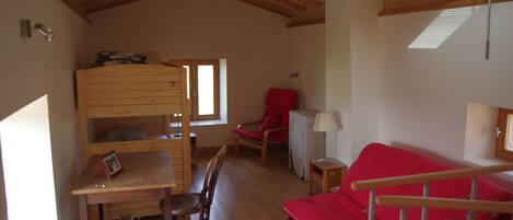 A cozy room with a bunk bed, a red sofa, a small table, and a chair.