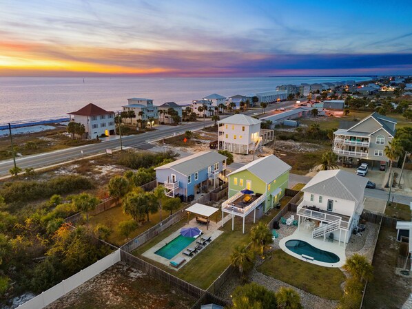 A coastal residential area with houses, a swimming pool, and a view of the ocean at sunset.