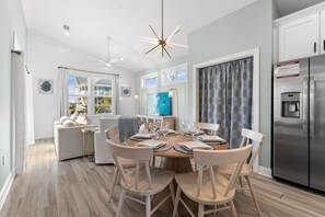 A modern kitchen with a dining area, featuring a central island, white cabinetry, and a stainless steel refrigerator.
