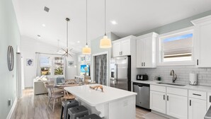 A modern kitchen with white cabinets, stainless steel appliances, and a large island with bar stools. - Luxe Coastal Dream w/Ocean Views + Private Pool (Port St. Joe)