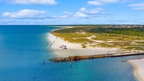 A coastal beach with clear blue waters, sandy shore, and a distant town. - Luxe Coastal Dream w/Ocean Views + Private Pool (Port St. Joe)