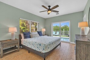Un dormitorio con cama, dos mesitas de noche, ventilador de techo y vistas al exterior.