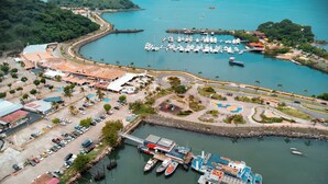 An aerial view of a marina with boats docked, a parking area, and surrounding greenery. - MARINN Tropical Vibes Hotel (Panama City)