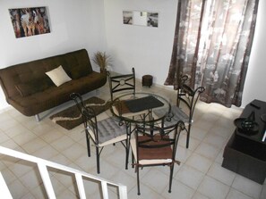 Un salon avec un canapé marron, une table basse en verre entourée de chaises, un petit tapis rond et une plante en pot.