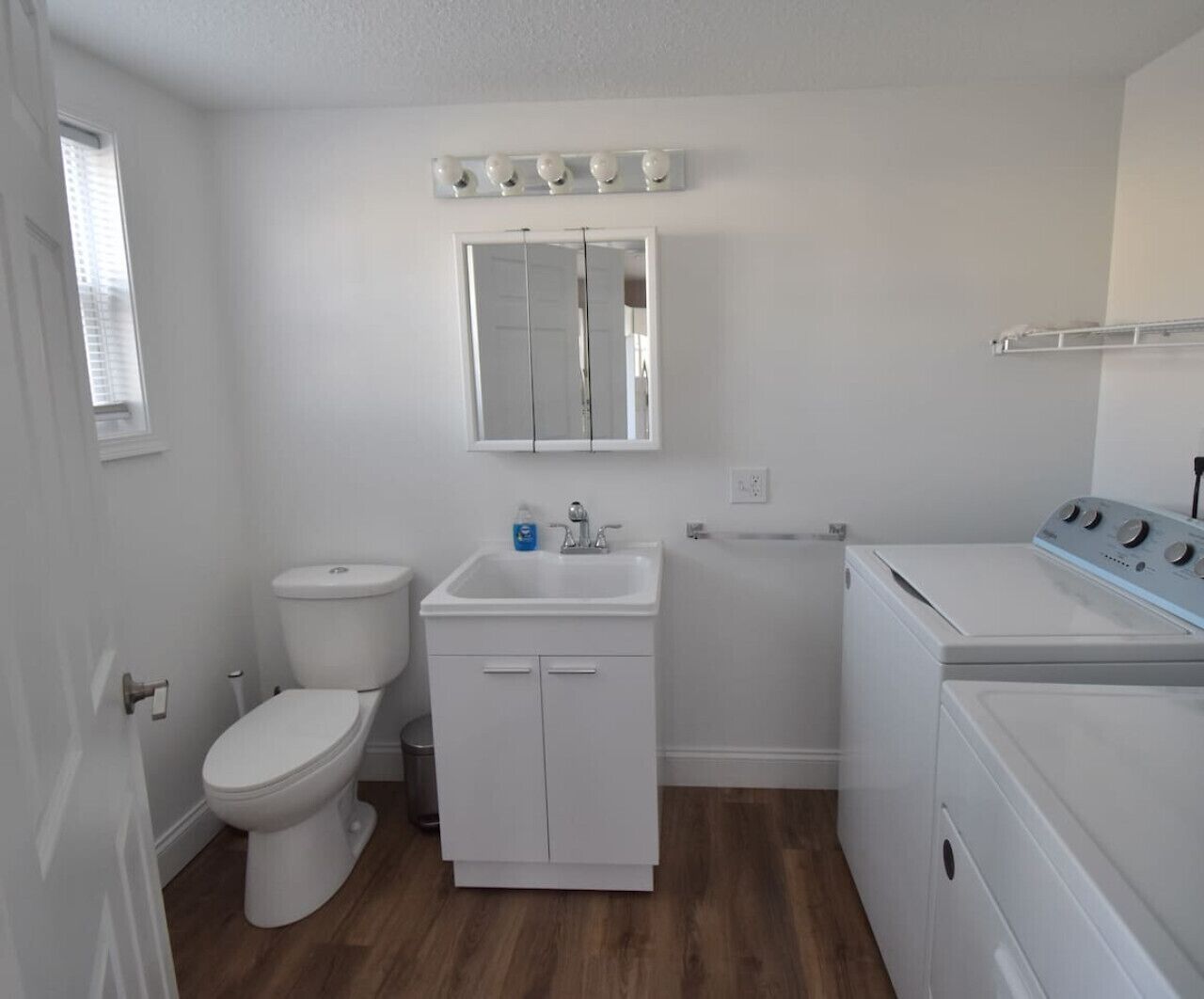 A compact bathroom with a toilet, sink, mirror, and washing machine.