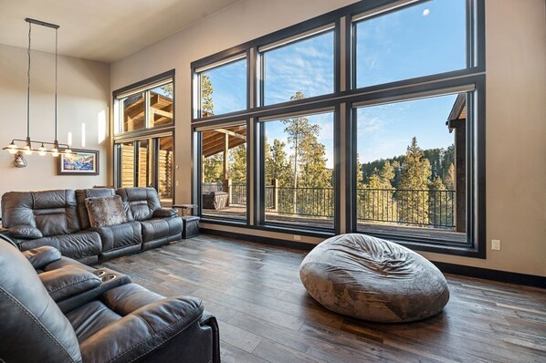 A spacious living room with a large sectional sofa, a bean bag, and a view of a balcony with a wooden deck and trees. - Family Friendly, Hot Tub, Clubhouse access, Ample parking room (South Lawrence)