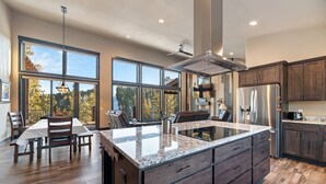 A spacious kitchen with a large island, dark wooden cabinets, and a view of the outdoors through large windows.