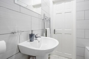 Bathroom features a white sink, mirror, and towel rack, set against a light grey tiled backdrop.