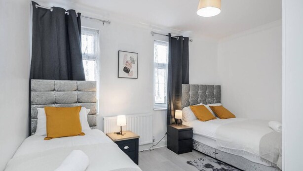 A hotel room with two beds, a radiator, a nightstand, a lamp, and a picture on the wall. - Stunning Top 2 Bed Flat Tilbury Central Location (Tilbury)