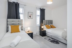 Two single beds with grey headboards and white bedding, set against a neutral backdrop with a grey rug and framed artwork.