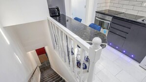 A modern kitchen with a black countertop, stainless steel appliances, and a white railing on the staircase. - Stunning Top 2 Bed Flat Tilbury Central Location (Tilbury)
