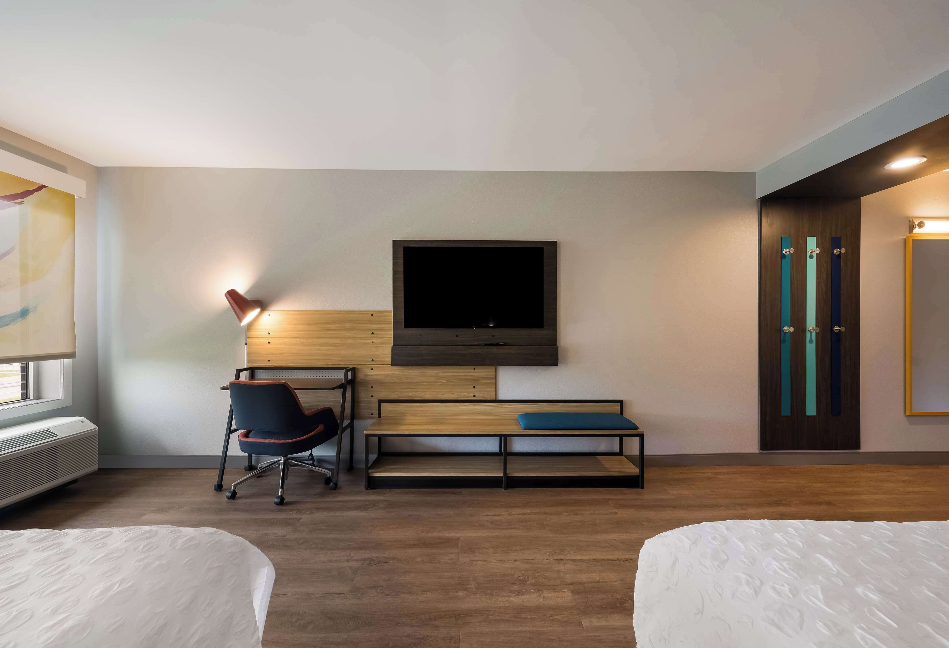 Een hotelkamer met twee bedden, een bureau met stoel, een aan de muur bevestigde televisie en een raam met een verwarming.