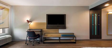Une chambre d’hôtel avec deux lits, un bureau avec une chaise, un téléviseur fixé au mur et une fenêtre avec un radiateur.