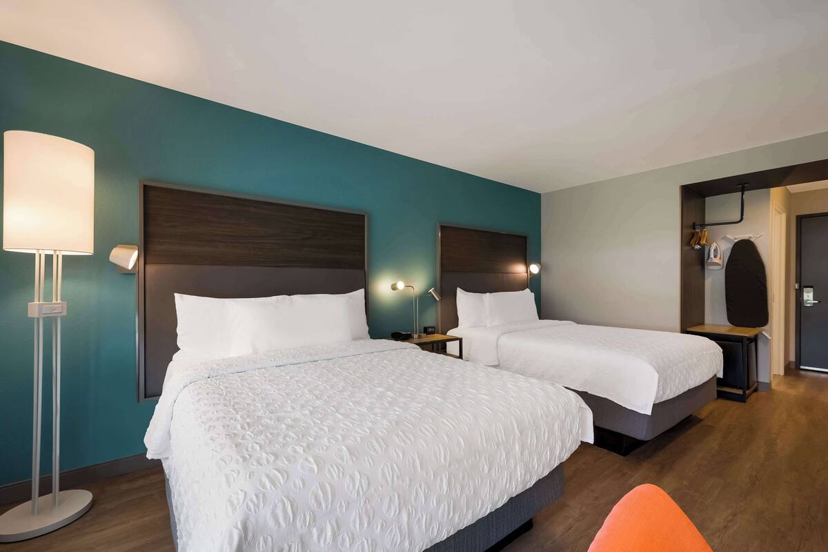 A hotel room with two beds, a standing lamp, and a small table with a lamp.