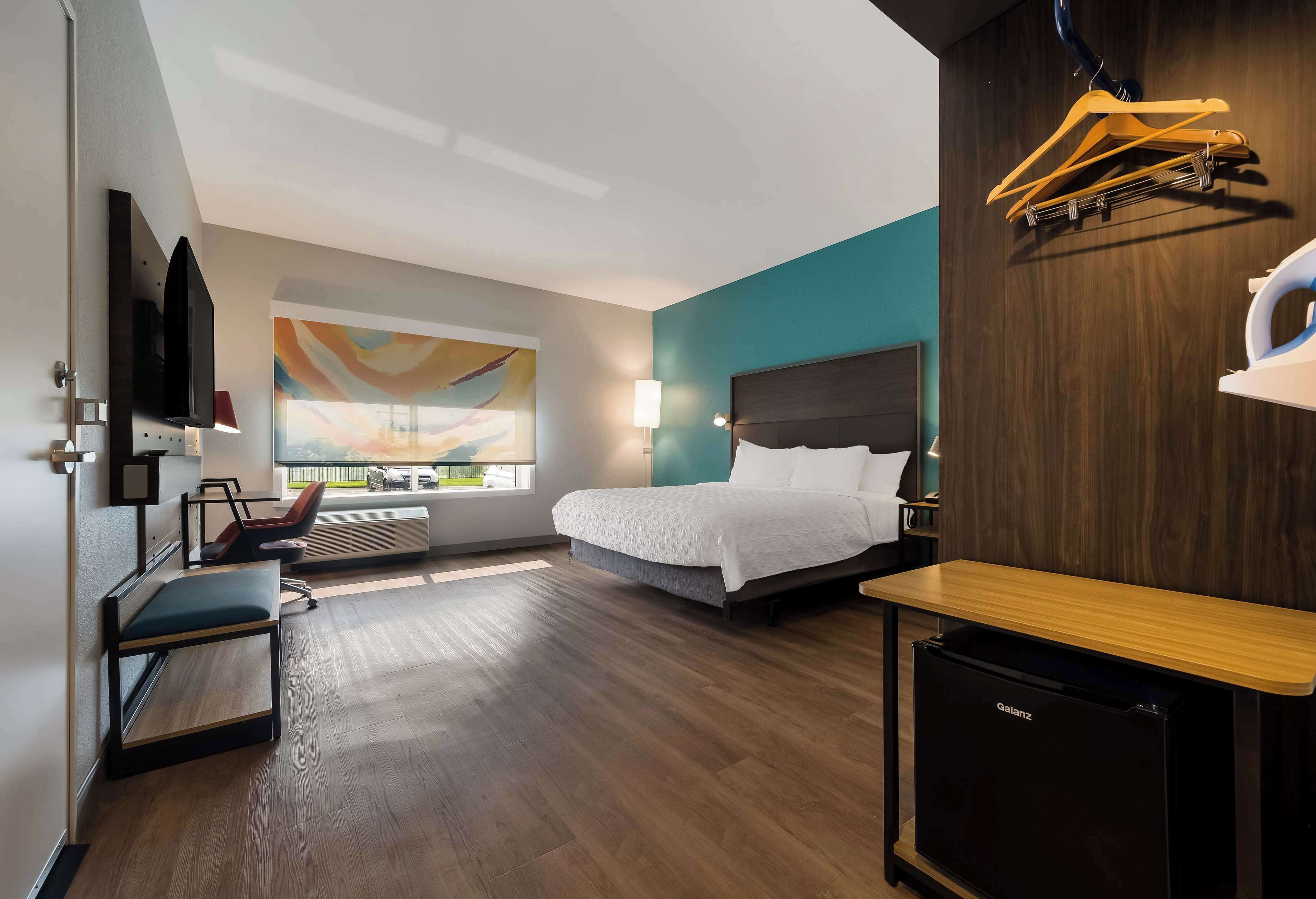 A modern hotel room with a bed, a desk, a chair, a TV, and a window with a view.