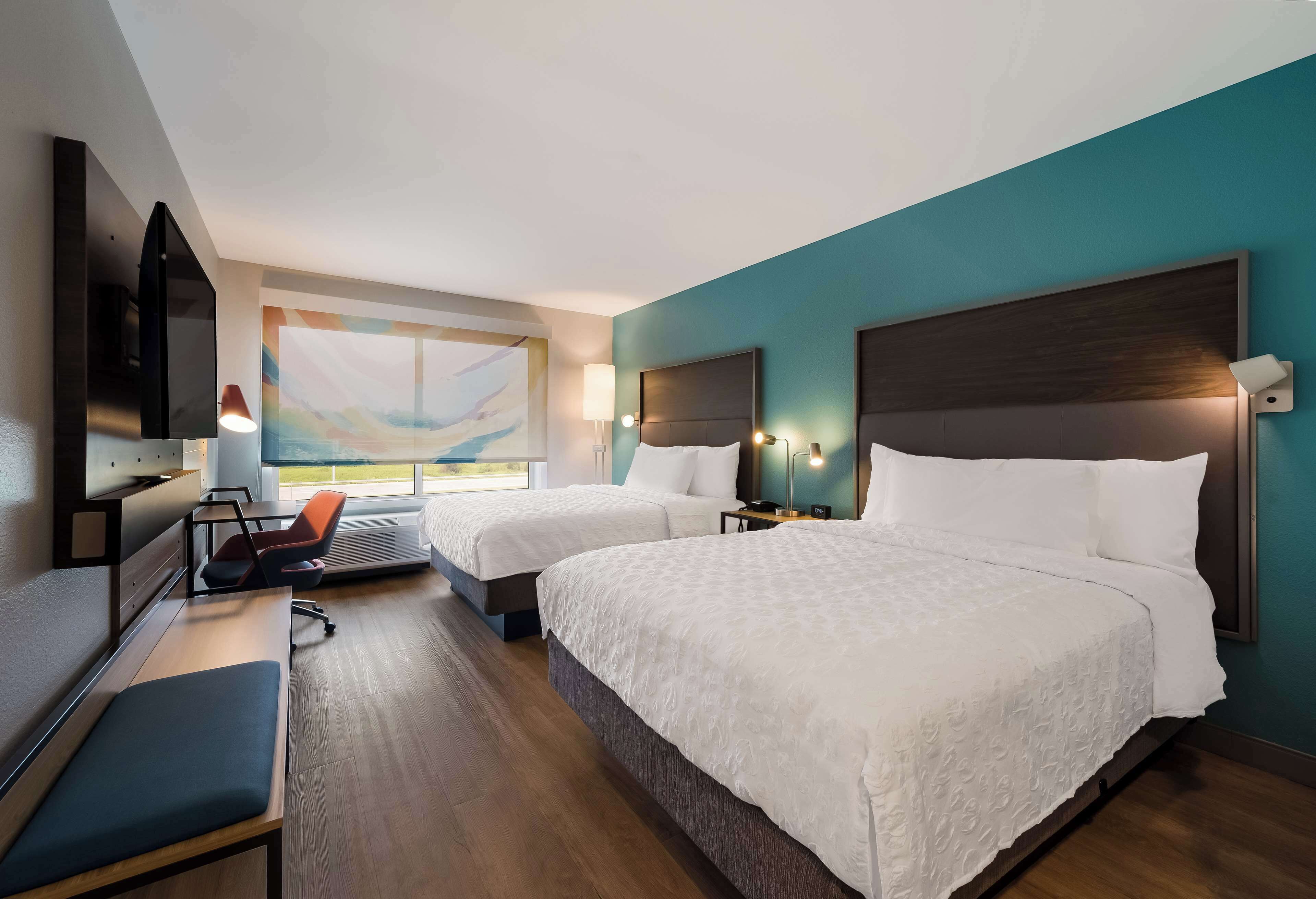 Quarto de hotel com duas camas, uma escrivaninha, uma cadeira, uma televisão e uma janela com vista.