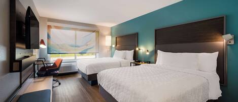 A hotel room with two beds, a desk, a chair, a TV, and a window with a view.
