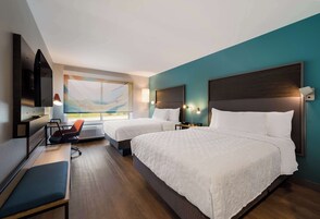Habitación de hotel con dos camas, un escritorio, una silla, un televisor y una ventana con vistas.