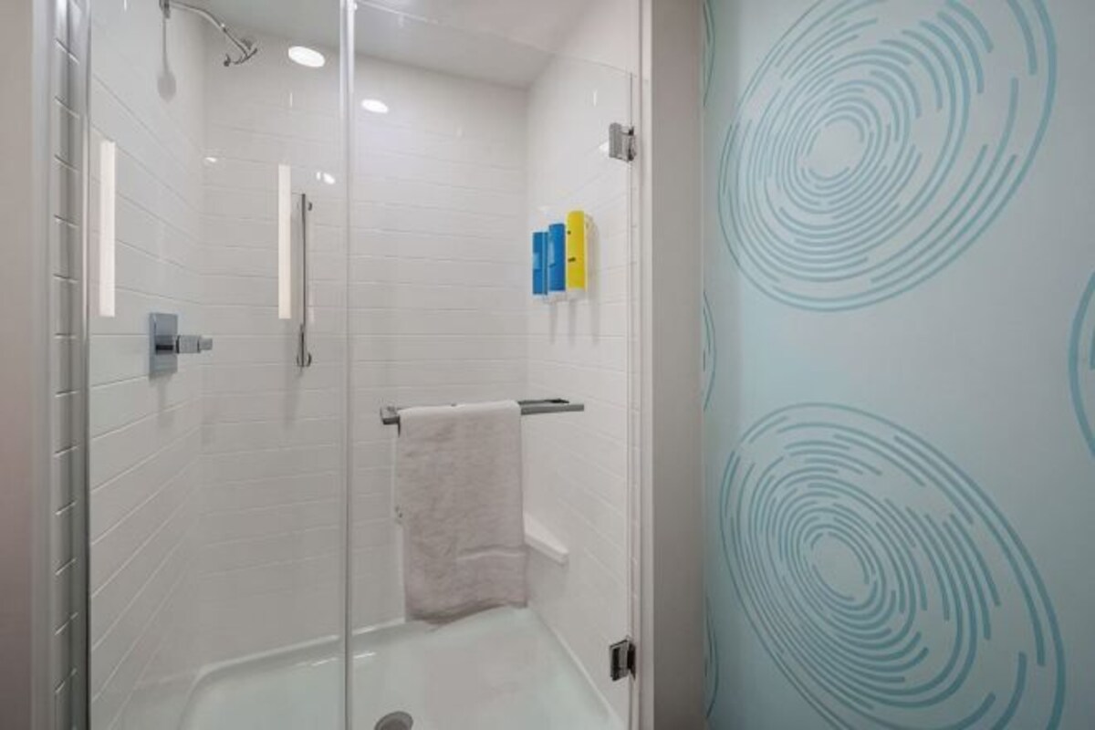 Une douche fermée par des parois de verre, avec une serviette blanche, des murs carrelés et un motif circulaire bleu sur le mur.