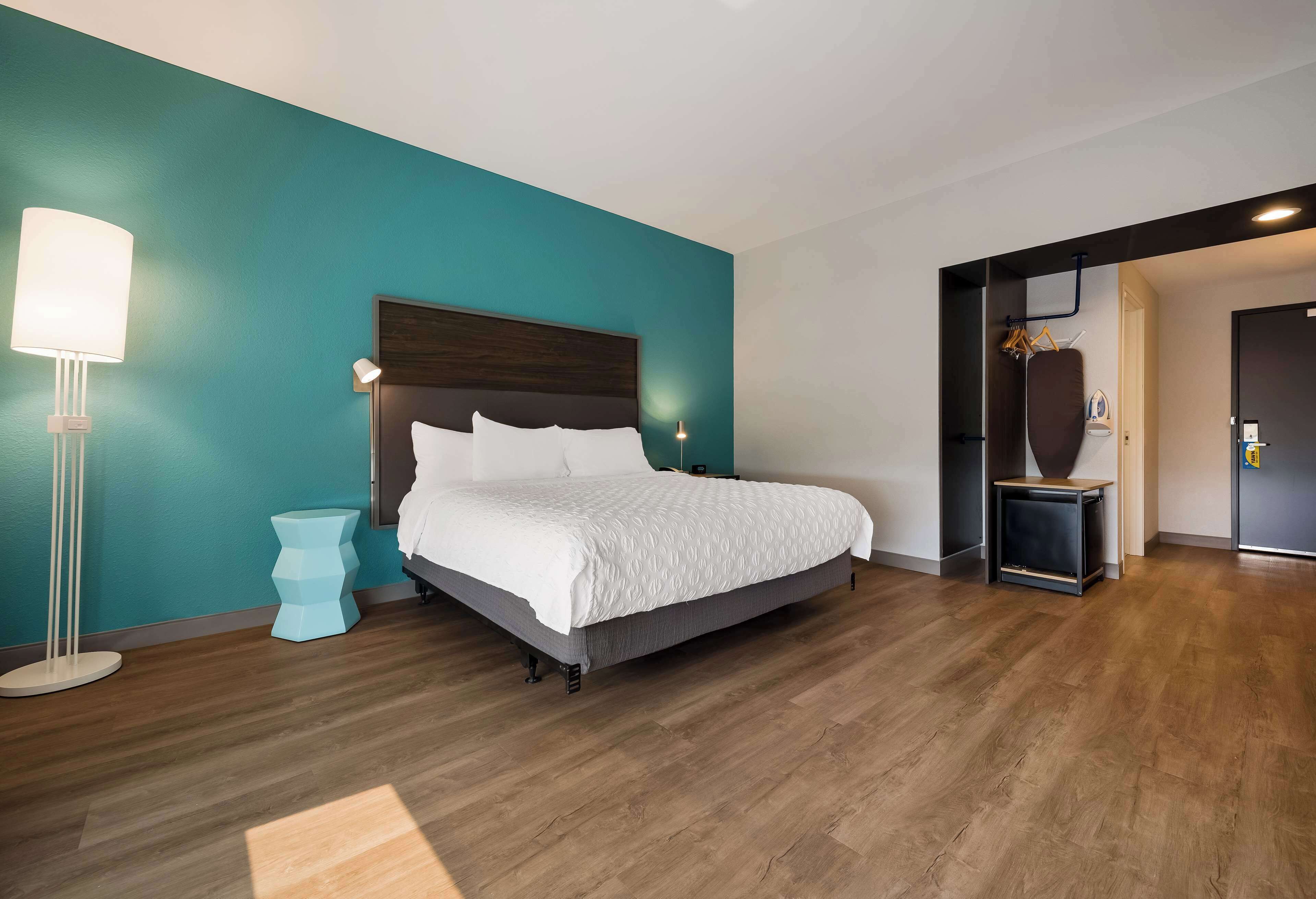 A modern hotel room with a large bed, a bedside table, a floor lamp, and a wardrobe.