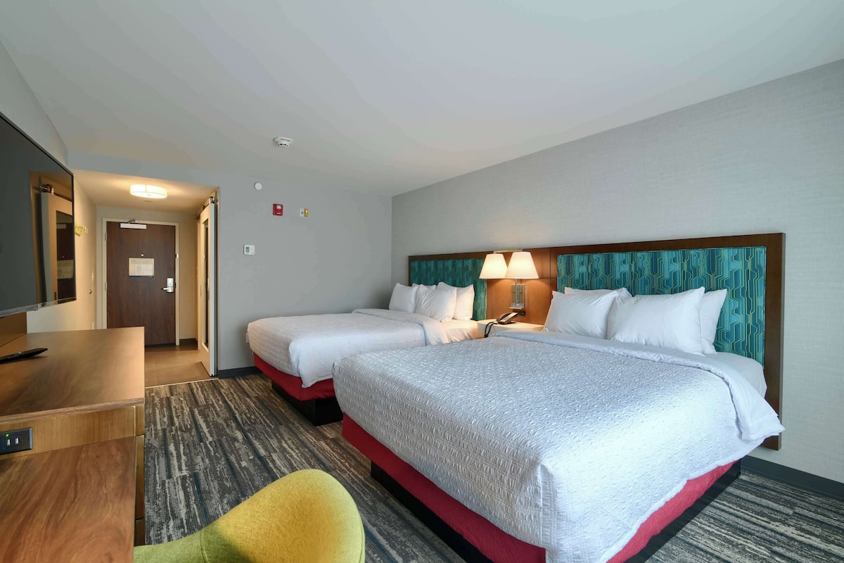 A hotel room with two beds, a desk, a chair, and a television.