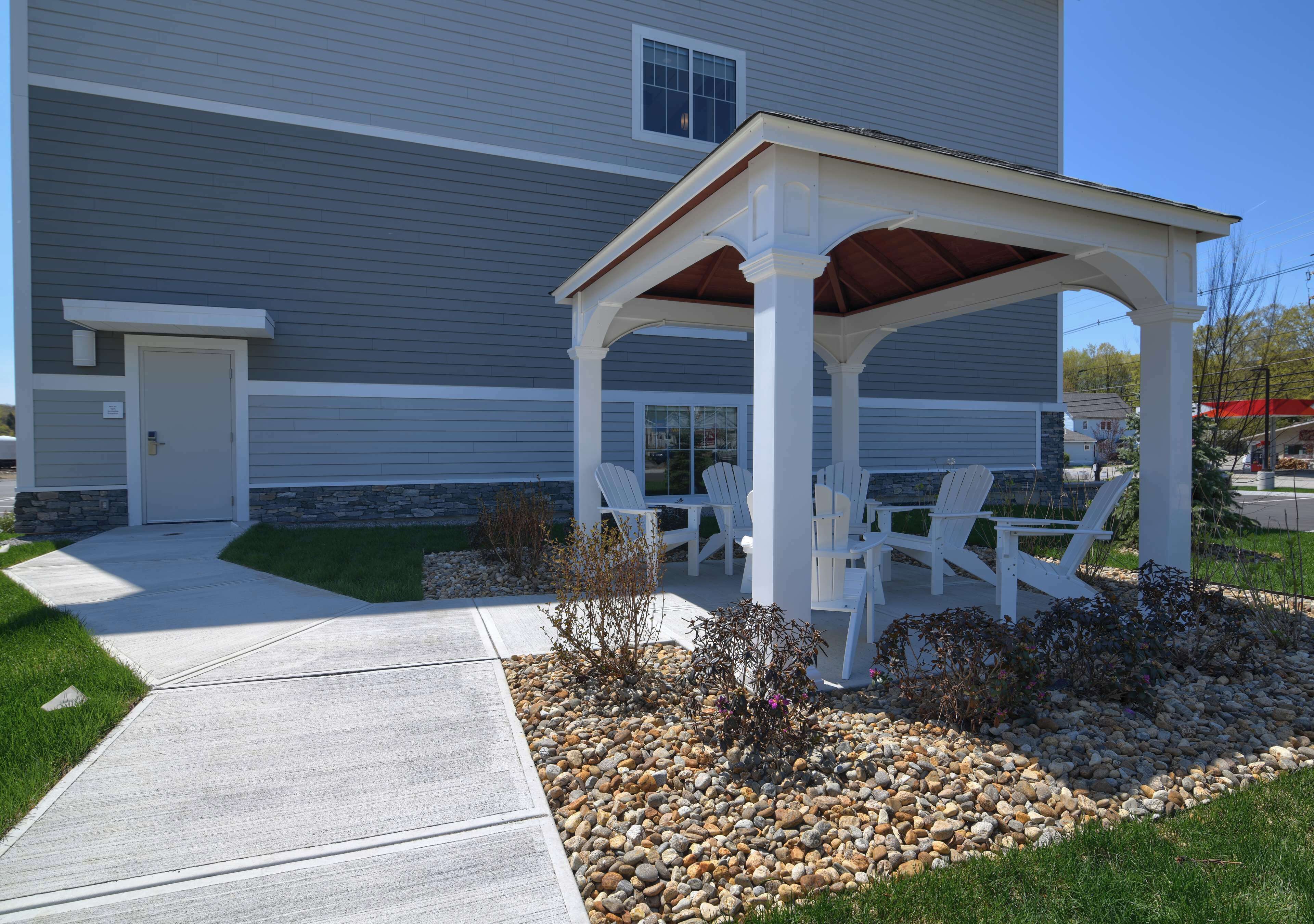A covered patio area with white chairs and a table, surrounded by a gravel and grass garden.