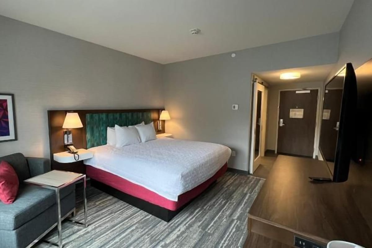 A hotel room with a bed, a desk, a chair, a TV, and a door.