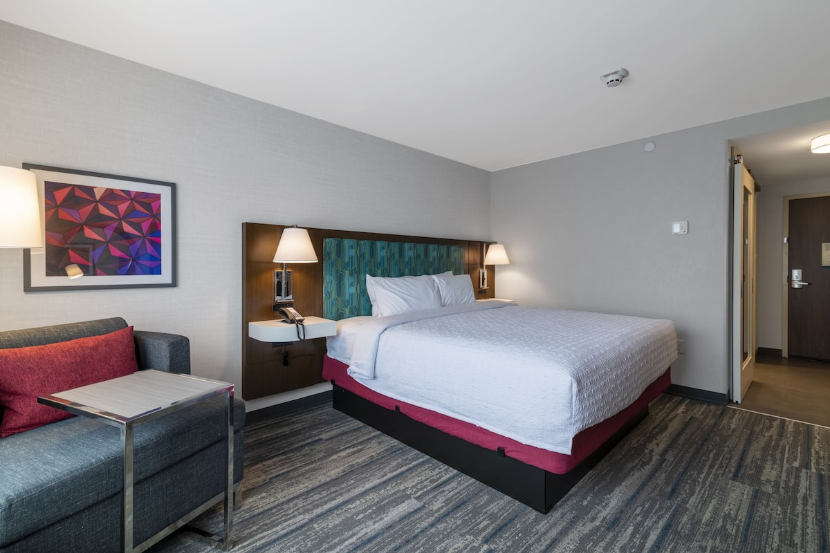 A hotel room with a bed, bedside table, lamp, and a wall-mounted phone.