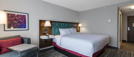 A hotel room with a bed, bedside table, lamp, and a wall-mounted phone.
