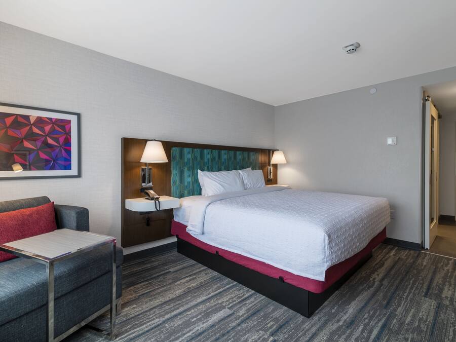 A hotel room with a bed, bedside table, lamp, and a wall-mounted phone.