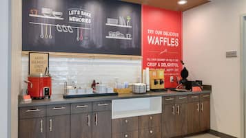 Una cocina moderna con una pared de pizarra que muestra alimentos para el desayuno y un letrero rojo que anuncia gofres.