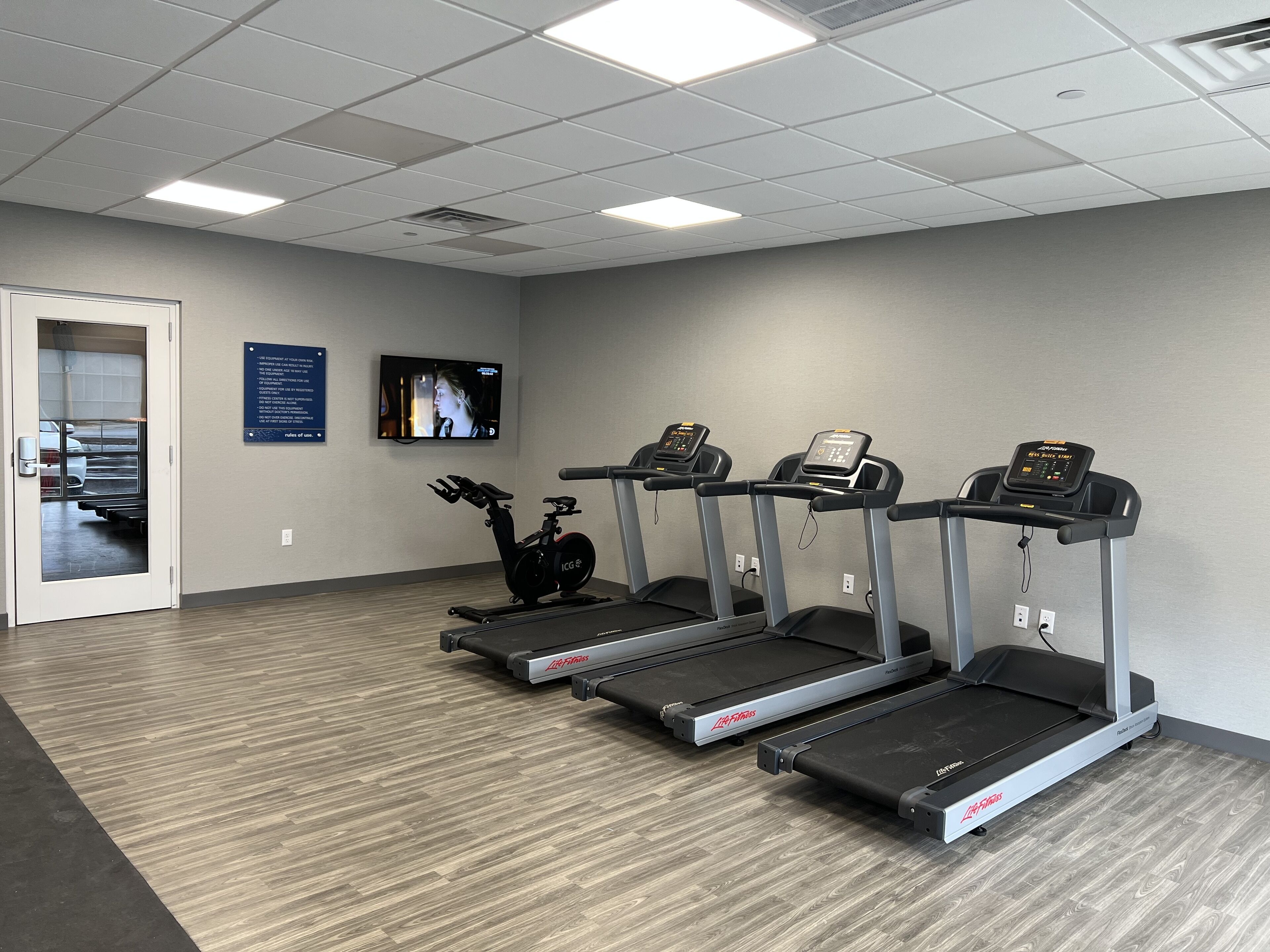 A fitness center with treadmills, a stationary bike, and a television screen displaying a workout video.