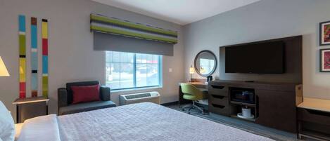 Une chambre d’hôtel avec un grand lit, un bureau avec une chaise, un téléviseur à écran plat, un miroir et une fenêtre avec des stores.