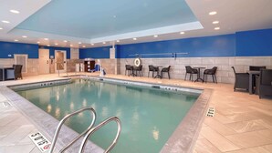 An indoor swimming pool with a blue ceiling, tiled walls, and a poolside area with chairs and tables. - Hampton Inn Lincoln White Mountains (Lincoln)