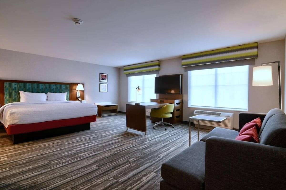 Ein Hotelzimmer mit Bett, Schreibtisch, Stuhl, Sofa und Fernseher.