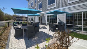 An outdoor patio with wicker furniture and blue umbrellas, adjacent to a building with large windows. - Hampton Inn Lincoln White Mountains (Lincoln)