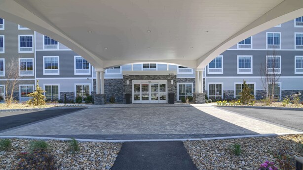 A covered entrance to a multi-story building with a stone facade and a central entrance. - Hampton Inn Lincoln White Mountains (Lincoln)