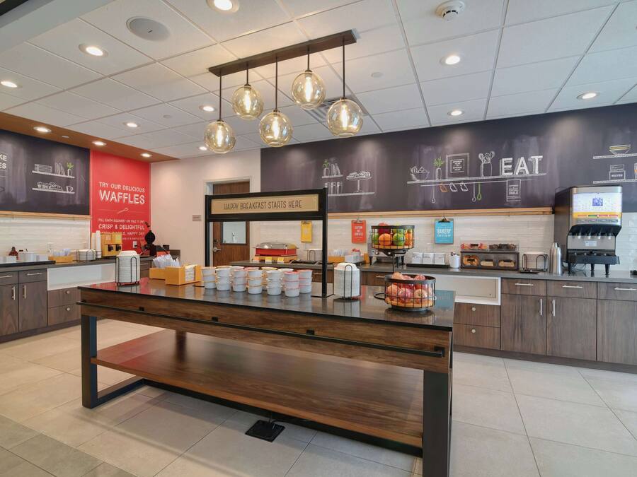 A modern cafe with a central counter, waffle station, and breakfast area.