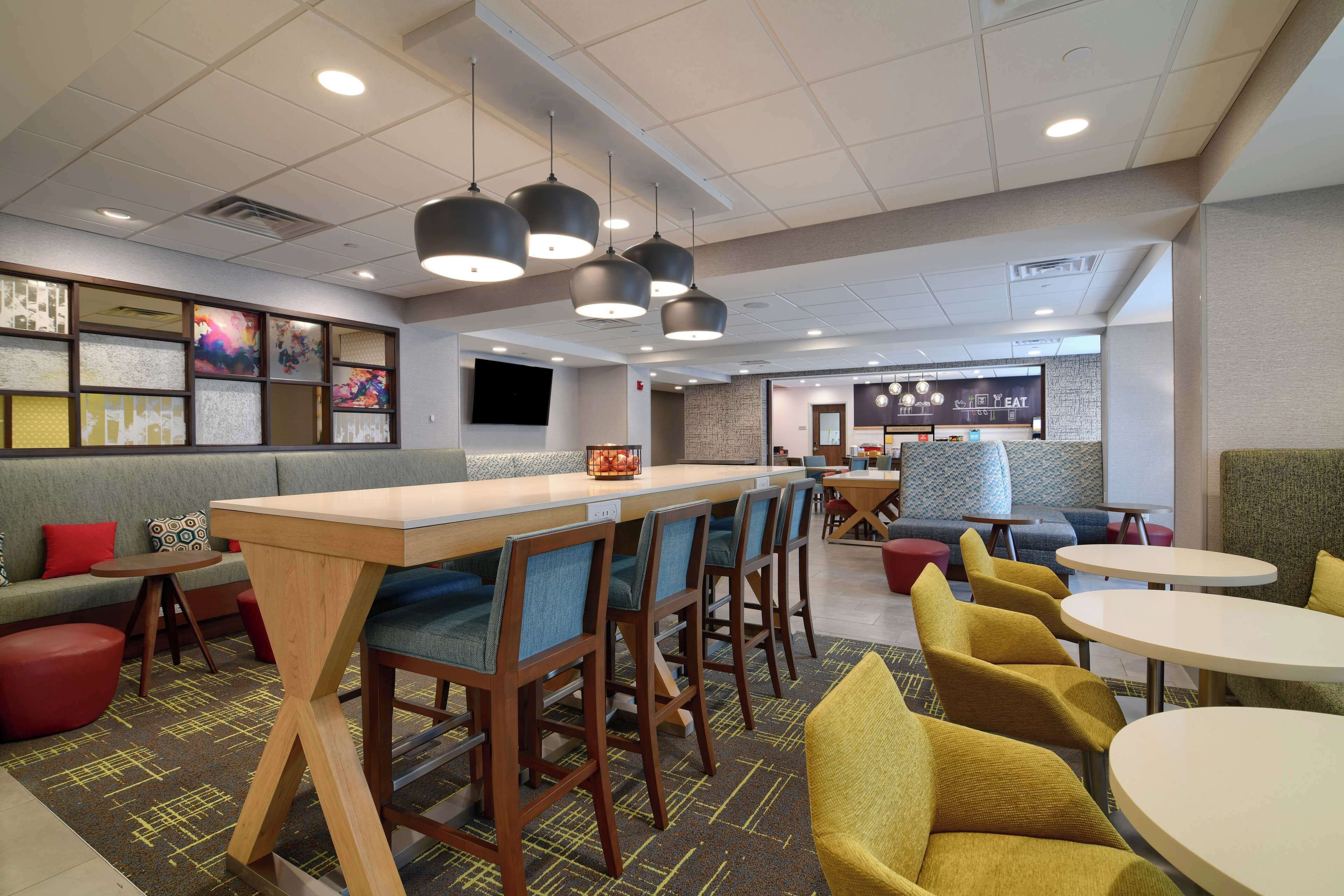 Een modern restaurant met een lange toonbank, barstoelen en ronde tafels.