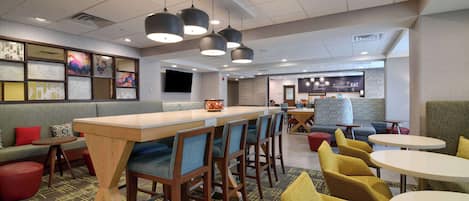 Een modern restaurant met een lange toonbank, barstoelen en ronde tafels.