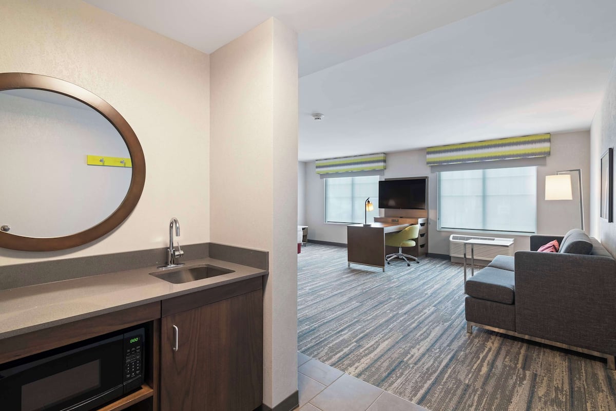 A modern hotel room with a kitchen area, a sofa, and a television.