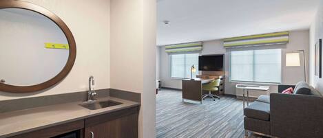 A modern hotel room with a kitchen area, a sofa, and a television.