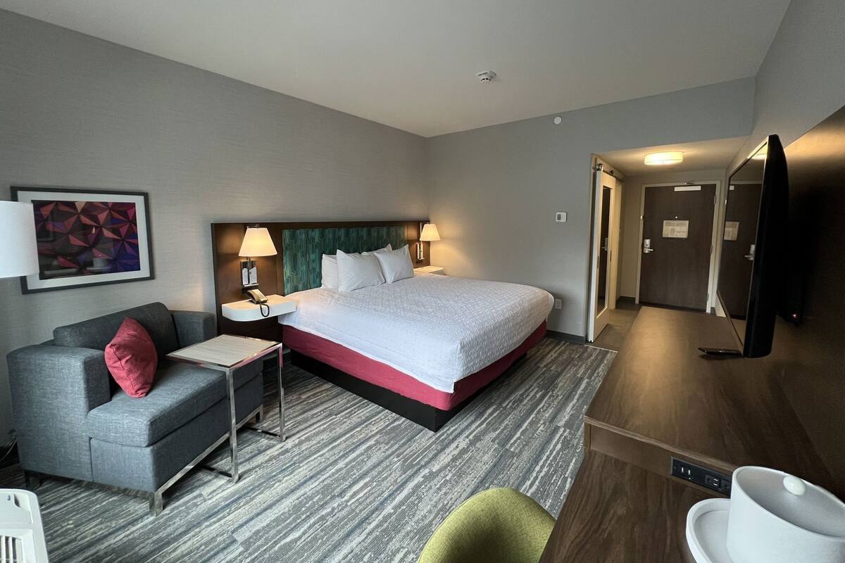 Ein Hotelzimmer mit Bett, Schreibtisch, Sessel, Sofa, Fernseher und Tür.