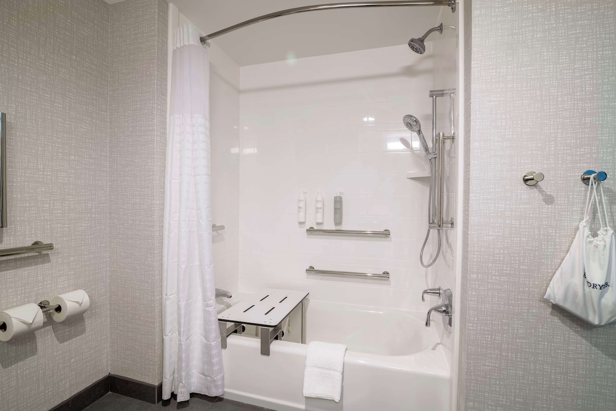 A modern bathroom with a bathtub, shower, and toilet paper dispenser.